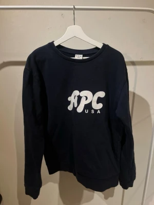 Mörkblå sweatshirt från A.P.C. - Snygg mörkblå sweatshirt från A.P.C. med vit logga på bröstet. Klassisk rund halsringning och ribbade muddar vid ärmslut och nederkant. Tillverkad i mjuk bomull för en skön och avslappnad look.