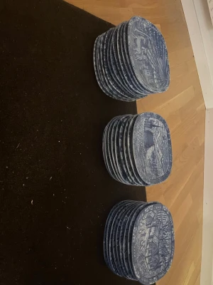 Blåvita tallrikar med motiv 1980 - Säljer ett gäng fyrkantiga tallrikar i porslin med blåvitt tryck och motiv av djur, hus och natur. Tallrikarna har detaljerade illustrationer och årtalet 1980 på framsidan. Perfekta för dig som gillar retro eller samlar på porslin med klassiska mönster. Skriv om du är intresserad och kanske inte skulle vilja köpa alla tallrikar på en och samma gång