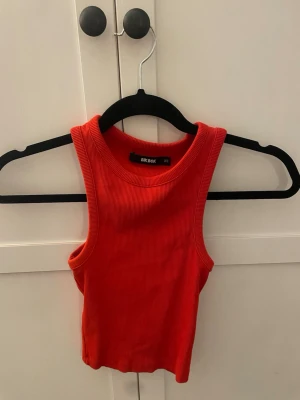 Röd ribbat linne från Bik Bok - Snygg röd ribbad linnetopp från Bik Bok i croppad modell. Toppen är ärmlös med breda axelband och rund halsringning. Perfekt att styla till jeans eller kjol för en trendig look.🥰💕