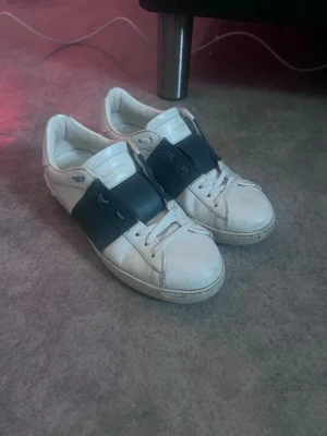 Valentino vita sneakers med mörkgrönt band - Snygga vita sneakers från Valentino med ett brett mörkgrönt band över vristen och klassisk låg siluett. Skorna har vita snören och diskret logga på plösen. Tillverkade i läder för en lyxig känsla och stilren look. Riktigt bra skick 8/10. Tyvärr ingen dustbag eller låda därav det billigare priset.
