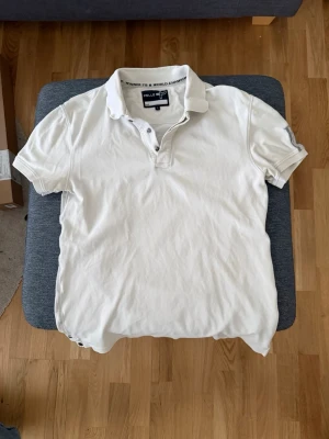 Vit pikétröja från Pelle P - Klassisk vit pikétröja från Pelle P med krage och knappar framtill. Tröjan har korta ärmar och diskret logga i nacken. Tillverkad i mjuk bomull som känns skön mot huden. Perfekt till jeans eller shorts för en clean look.