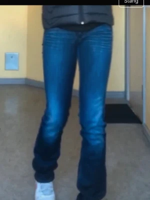 Blå bootcut jeans från Nudie Jeans - Säljer ett par klassiska blå bootcut jeans från Nudie Jeans med snygga slitningar och kontrastsömmar. Jeansen har fem fickor, normal midja och vågigt broderi på bakfickorna. Perfekta för dig som gillar en avslappnad men trendig look.