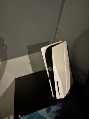 PlayStation 5 spelkonsol - Säljer en PlayStation 5 från Sony. Konsolen har en futuristisk design med vita och svarta paneler och en vertikal form. Materialet är plast med en matt och blank finish. Perfekt för gaming och streaming.