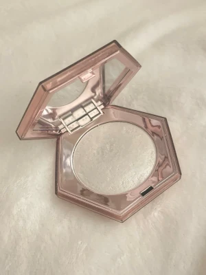 Fenty Beauty highlighter How many carats - Supersnygg highlighter från Fenty Beauty i en glansig, roséguldig hexagonformad dosa med spegel. Själva highlightern är vit med en skimrande finish som ger ett riktigt glow. Perfekt för att framhäva kindben och ge extra lyster till din look. Skickas nästa vardag.  Oanvänd, endast swatchad. Obs: den är 2 år gammal. Skick enligt bild. 