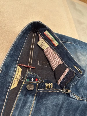 Blå jeans Jacob Cohen 711 - Snygga blå jeans från Jacob Cohen, modell 711. Jeansen har klassisk femficksdesign, gul kontrastsöm och unika detaljer som färgade nitar och mönstrat innerfoder. Tillverkade i mjuk denim med lätt tvättad look och raka ben. straight. liten svart prick på backfickan