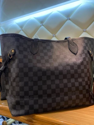 Rutig shoppingväska  - Stilren shoppingväska i svart rutigt mönster. Väskan har två handtag, detaljer i skinn och klassisk öppen topp. Perfekt för dig som vill ha plats för allt och samtidigt se trendig ut.