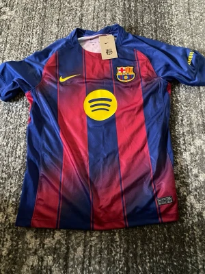 FC Barcelona matchtröja Lamine Yamal - Säljer en officiell FC Barcelona matchtröja från Nike med Lamine Yamal och nummer 10 på ryggen. Tröjan har klassiska blå och röda ränder, klubbmärke, Nike-logga och Spotify som sponsor framtill. Tillverkad i lätt och ventilerande material, perfekt för fotbollsträning eller match.