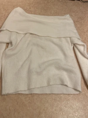 Vit off shoulder stickad tröja - Säljer en vit stickad tröja med off shoulder-design och bred krage. Tröjan har långa ärmar och ribbstickade muddar vid nederkant och ärmslut. Perfekt för dig som vill ha en stilren och trendig look.