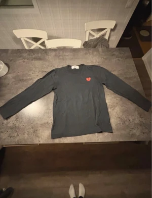 Cdg långärmad tröja - Säljer en svart långärmad topp från Comme des Garçons Play med det ikoniska röda hjärtat broderat på bröstet. Klassisk rund halsringning och mjukt bomullsmaterial som är skönt mot huden. Perfekt för dig som gillar stilrena plagg med en twist.