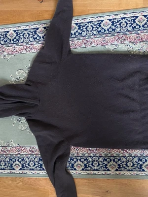 Mörkgrå hoodie med huva - En enkel och stilren mörkgrå hoodie med huva. Hoodien har långa ärmar och ribbade muddar vid ärmslut och nederkant. Perfekt för en avslappnad look och passar till det mesta. Materialet känns mjukt och bekvämt mot huden.