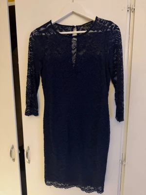 Marinblå spetsklänning från New Look - Säljer en marinblå spetsklänning från New Look med trekvartsärm och rund halsringning. Klänningen har vackra spetsdetaljer över hela och en liten öppning vid halsen. Perfekt för dig som gillar elegant och stilren design.