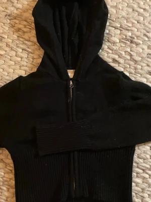 Svart hoodie med dragkedja Gina Tricot - Säljer en svart hoodie från Gina Tricot med dragkedja framtill och ribbade muddar. Hoodien har en klassisk huva och är gjord i mjukt material.