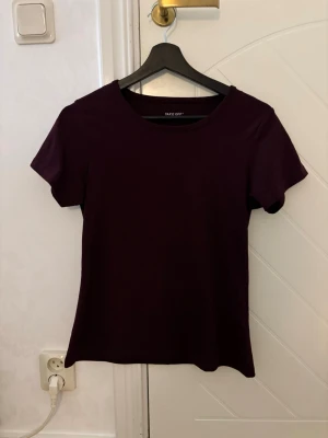 Mörklila t-shirt från Take Off - En stilren mörklila t-shirt från Take Off med rund halsringning och korta ärmar. T-shirten har en enkel och clean design som passar perfekt till jeans eller kjol. Tillverkad i mjukt material för skön känsla hela dagen.