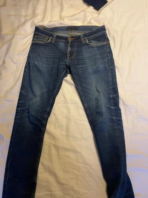Nudie jeans - Snygga blå jeans från Nudie Jeans med klassisk orange söm på bakfickorna. Modellen är slim fit med smal passform och normal midja. Jeansen har slitningar på ena benet och är tillverkade i mjukt denimtyg. Nu pris runt 1600