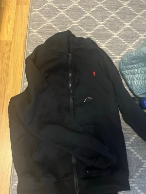  Ralph Lauren tracksuit - Säljer ett par svarta mjukisbyxor från Ralph Lauren med den klassiska röda loggan broderad på benet. Byxorna har en avslappnad passform och är gjorda i mjukt bomullsmaterial. Perfekta för chill dagar eller när du vill vara extra bekväm.