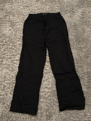 Svarta linnebyxor med snörning - Oanvända svarta linnebyxor med avslappnad passform och snörning i midjan. Byxorna har elastisk midja och en bakficka. 