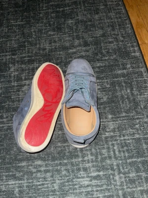 Louboutin skor  - Säljer ett par stilrena blå sneakers i mocka med ljusblå snörning och vit mellansula. Skorna har en unik röd yttersula och klassisk låg profil. Perfekta för dig som vill ha något lite annorlunda till din outfit. Pris kan diskuteras vid snabb affär!