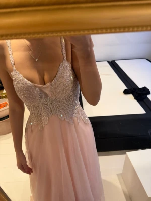 Ljusrosa långklänning med paljetter - Elegant ljusrosa långklänning med smala axelband och v-ringning. Överdelen är dekorerad med glittriga paljetter i ett blommigt mönster och kjolen är i ett tunt, flygigt material som ger en romantisk känsla. Perfekt för bal eller fest.