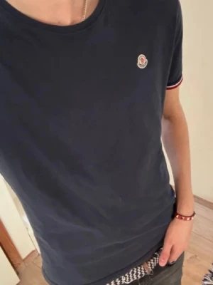 Mörkblå Moncler t-shirt med logga - Säljer en äkta monclear tischa som är riktigt fet, hör av er vid frågor och funderingar. Obs det är två små hål i tröjan där bak syns inte dock. Lappen är avriven och kvitto kommer inte med!