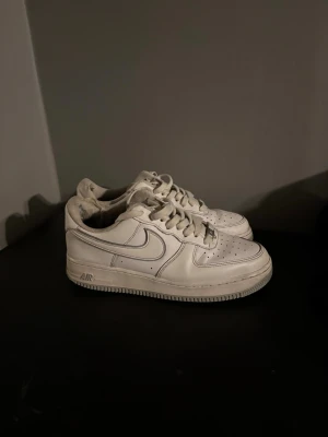 Nike Air Force 1 vita sneakers - Klassiska Nike Air Force 1 sneakers i helvitt skinn med perforerad tå, rund tå och snörning. Snygg och tidlös modell med låg profil och tydlig Nike-logga på sidan och hälen. Perfekta för dig som gillar streetwear och vill ha en ikonisk sneaker i garderoben.