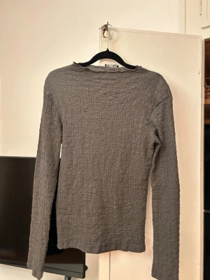 Grå ribbad långärmad topp Zara - Säljer en grå långärmad topp från Zara med ribbad struktur. Toppen har en enkel, rak passform och är tillverkad i ett mjukt material som känns skönt mot huden. Perfekt att styla med jeans eller kjol för en clean look.