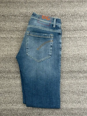 Blå George Dondup jeans - Säljer ett par blå George jeans från Dondup. Jeansen har en snygg tvätt och kontrastsömmar på bakfickorna. Perfekta för en trendig och avslappnad look. Bra skick, inga defekter, äkta!