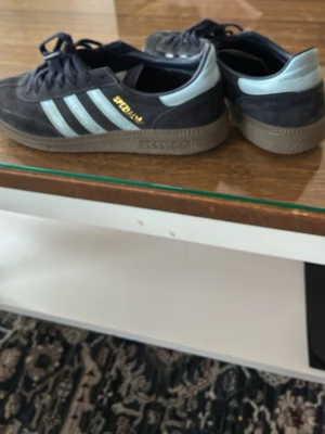 Adidas Spezial sneakers mörkblå ljusblå - Säljer ett par Adidas Spezial sneakers i mörkblå mocka med ljusblå detaljer och klassiska tre ränder på sidan. Gummisula i brunt och guldfärgad Spezial-text på sidan. Perfekta för dig som gillar retrostil och streetwear.
