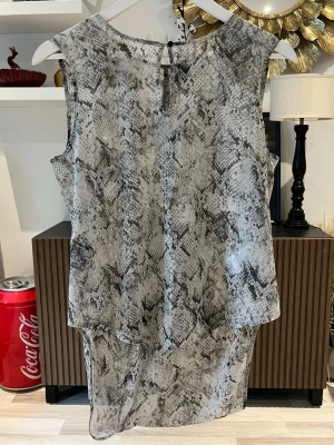 Ärmlös topp med ormmönster - Säljer en snygg ärmlös topp med grått och svart ormmönster från gina tricot i storlek S. Toppen har rund halsringning och ett lätt transparent material som ger en luftig känsla. Perfekt för dig som vill ha ett djuriskt print. Axelbredd: 36cm. Längd: 74cm. Byst: 50cm.