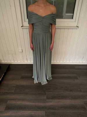 Ljusgrön off shoulder långklänning - Säljer en elegant ljusgrön långklänning med off shoulder-design och draperad överdel. Klänningen har ett flödande fall och markerad midja, perfekt för dig som vill ha en stilren och modern look. Materialet känns mjukt och följsamt mot kroppen. Den är i en storlek 36 men den är super stretchig i materialet så passar allt från 32-38. 