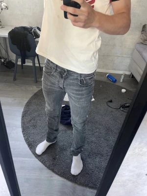 Grå slim fit jeans från Replay - Snygga grå slim fit jeans från Replay med klassisk femficksmodell och slitna detaljer. Jeansen har en något tvättad look och är tillverkade i mjukt denimtyg med stretch för extra komfort. Perfekta för en avslappnad och trendig stil.