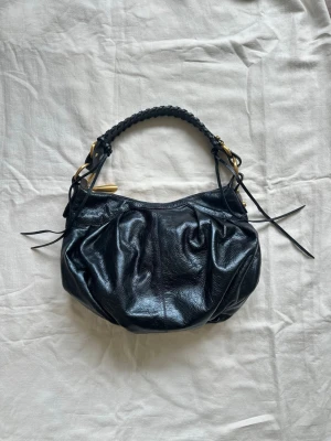 Väska  - Mörkblå väska från det exklusiva märket Francesco Biasia, väskan är sällsynt och vintage. Den har en flätad axelrem, guldfärgade metalldetaljer och dekorativa knytband på sidorna. 39x29cm, vid köp av flera varor får du rabatt 💛