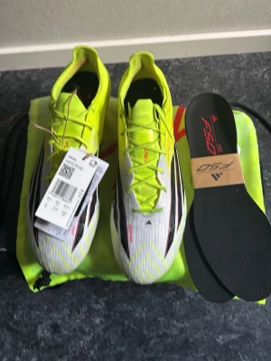 Adidas F50 Elite AG fotbollsskor - Säljer ett par Adidas F50 Elite AG fotbollsskor i vitt och neongult med svarta detaljer. Skorna har en modern, strömlinjeformad design och levereras med extra innersulor och en matchande neongul påse. Perfekta för spel på konstgräs. Och de är använda 2 träningar