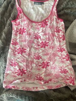 Blommig linnetopp från Race Marine - Säljer en söt linnetopp från Race Marine i vitt med rosa blommigt mönster. Toppen är ärmlös med rundad halsringning och har rosa kantband. Perfekt för varma dagar och enkel att matcha med jeans eller shorts.