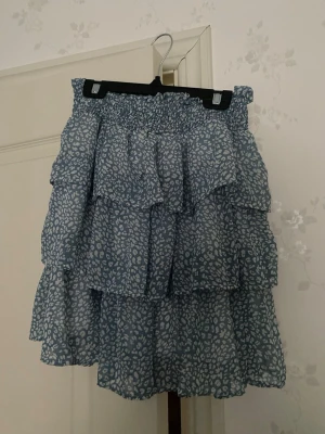 Blå volangkjol med mönster - Kort volangkjol av märket By Clara Paris med resår i midjan. Aldrig använd så nyskick