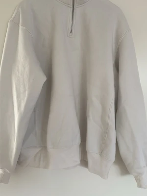 Vit halvzip hoodie - En stilren vit hoodie med halv dragkedja framtill och ribbade muddar vid ärmslut och nederkant. Hoodien har en relaxed passform och är tillverkad i mjukt bomullsmaterial. 
