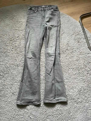 Grå bootcut jeans från LAB Industries - Säljer ett par grå bootcut jeans från LAB Industries. Jeansen har klassisk femficksdesign, bälteshällor och knappgylf. Materialet är denim i bomull och passformen är utsvängd nedtill för en trendig look.
