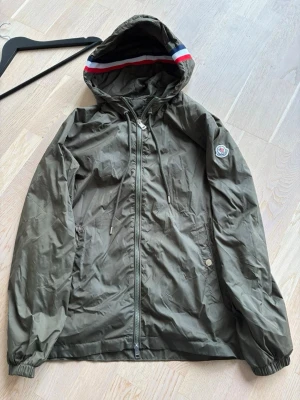 Moncler Windbreaker - Snygg och stilren Moncler windbreaker i militärgrön färg. Perfekt som lätt jacka för vår, sommar och höst. Strl 2 (S) en riktigt clean och enkel windbreaker som funkar till allt. NFC tag finns inuti jackan!