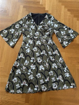 Blommig omlottklänning från Stockh LM - Snygg grön omlottklänning från Stockh LM med vitt och rosa blommönster. Klänningen har trekvartsärmar, v-ringning och knyt i midjan. Perfekt för dig som gillar en feminin och trendig stil.