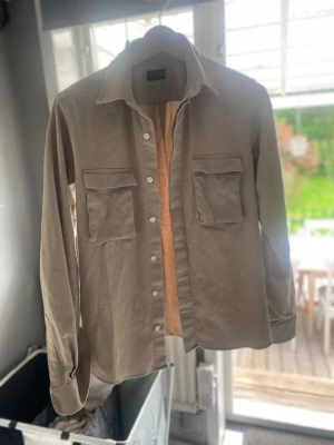 Rose & born Overshirt - Säljer en Rose & Born Overshirt i beige. Materialet är bomull av högata kvalitet. Storleken är 46 (Small) och skicket är mycket bra. Hör av dig vid intresse!