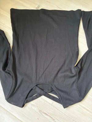 Svart ribbad tröja  - Långärmad tröja med ribbat tyg och ett kors i övre ryggen. Köpt på Lindex för längesen. Storlek: 146/152 eller XS/S