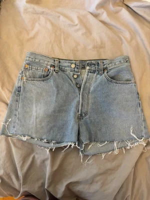 Levi's ljusblå jeansshorts med fransar - Ljusblå jeansshorts från Levi's, fransiga benslut och klassiska fem fickor. Knappar framtill och Levi's-patch bak i midjan. Perfekta för sommaren.    Storlek: W32 L 32