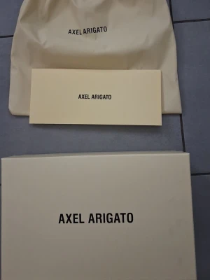 Svarta Axel Arigato sneakers - Stilrena svarta sneakers från Axel Arigato med vit tjock sula och diskret logga på sidan. Skorna har en klassisk låg profil och är tillverkade i mocka för en lyxig känsla. Perfekta för dig som gillar minimalistisk och modern design. Priset kan diskuteras .