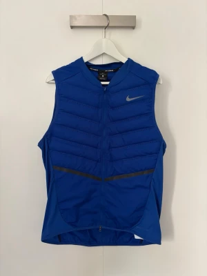 Blå Nike Aeroloft dunväst - Snygg blå dunväst från Nike Aeroloft-kollektionen, perfekt för löpning. I storlek L men skulle säga att den passar M också. Priset är förhandlingsbart så det är bara att buda på.