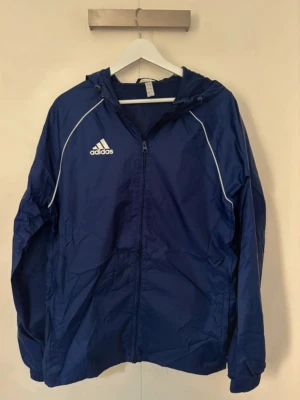 Blå vindjacka från Adidas - En snygg adidas windbreaker i marinblå och vit färg, den är i storlek M.Priset är förhandlingsbart så det är bara att buda.