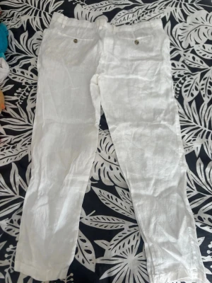 Vita linnebyxor från Dressmann - Snygga vita linnebyxor från Dressmann i 100% linne. Byxorna har raka ben, två framfickor med knappdetaljer och klassisk midja. Perfekta för en avslappnad och stilren look under varma dagar.