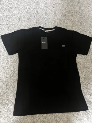 Svart t-shirt  - Snygg svart t-shirt med diskret logga på bröstet. Klassisk passform och rund halsringning. Tillverkad i mjuk bomull som känns skön mot huden. Perfekt basplagg för en stilren look.