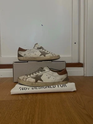 Golden Goose vita sneakers med stjärna - Golden Goose sneakers i vitt läder med den ikoniska grå stjärnan på sidan och bruna detaljer vid hälen. 