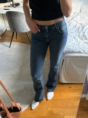 Blå bootcut jeans med medelhög midja - Säljer ett par blå bootcut jeans med klassisk femficksdesign. Jeansen har en snygg tvätt och lätt utsvängda ben, perfekta till sneakers eller boots. Materialet är stretchigt denim som sitter bekvämt hela dagen.