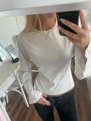 Vit croppad topp med knyt i ryggen Nelly - Trendig vit långärmad topp med croppad passform och snygg knytning i ryggen. Kommer ifrån Nelly, storlek XXS, knappt använd, slutsåld.