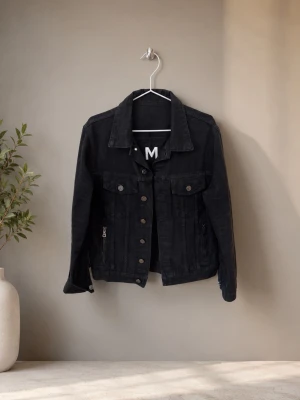 Svart jeansjacka från Balmain - Snygg svart jeansjacka från Balmain med klassisk krage, knappar framtill och två bröstfickor. På ryggen finns en stor vit BALMAIN-logga som ger jackan en exklusiv känsla. Perfekt för dig som vill sticka ut med en trendig och tidlös look.